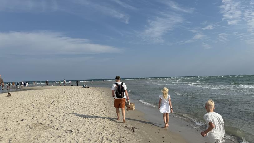 En man och två barn går längs havet på en vit strand i Danmark