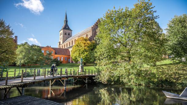 Fietsers rijden over de brug naar de sprookjestuin in Odense met de Odense Domkirke als achtergrond