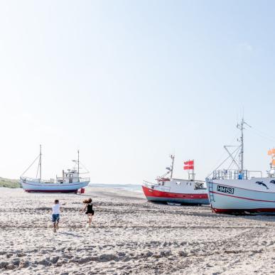 Barn som løper på stranden ved fiskebåter i Danmark